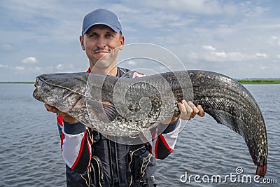 Happy fisherman with big catfish fish trophy at the boat with fishing tackles Stock Photo