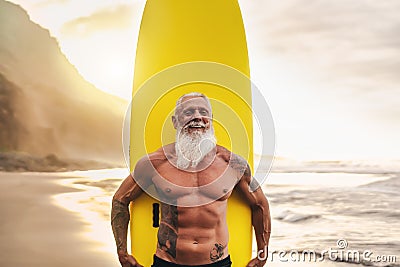 Happy fit senior having fun surfing at sunset time - Sporty bearded man training with surfboard on the beach Stock Photo