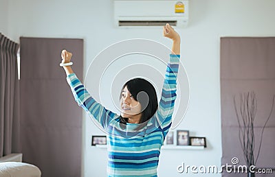 Happy fresh woman hands up and standing in front switching of the air conditioner Stock Photo
