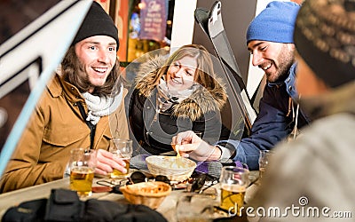 Happy friends drinking beer and eating chips at ski resort chalet Stock Photo