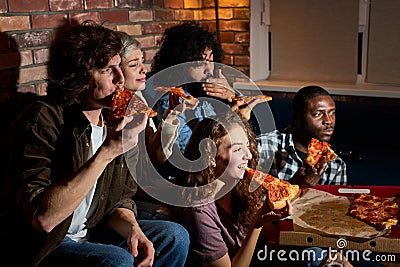 friendship, people, entertainment and junk food concept - happy friends eating pizza and watching movie or tv series at Stock Photo