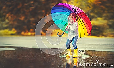 Happy funny child girl with umbrella jumping on puddles in rubb Stock Photo