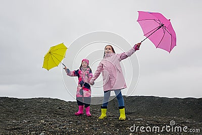 Happy funny children with pink and yellow umbrella outdoors. Girls wearing pink raincoat and enjoying rainfall. Stock Photo