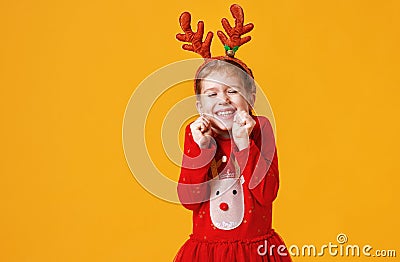 Happy funny emotional child girl in red Christmas reindeer costume on yellow background Stock Photo