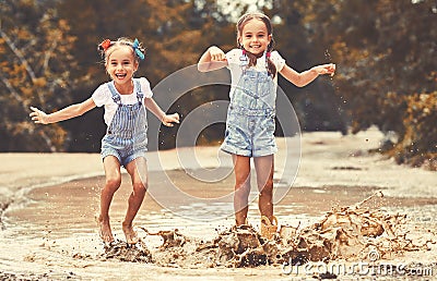 Happy funny sisters twins child by girl jumping on puddles and laughing Stock Photo