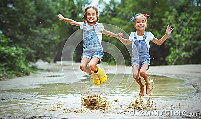 Happy funny sisters twins child girl jumping on puddles in rub Stock Photo