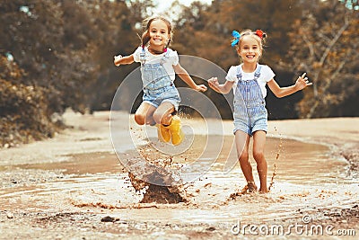 Happy funny sisters twins child girl jumping on puddles in rub Stock Photo