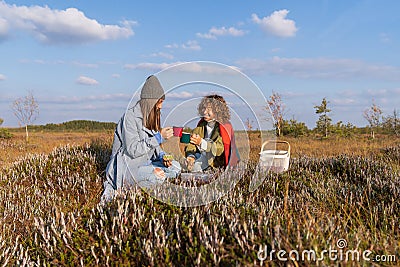 Happy girl best friends drink hot tea in mugs sitting on swamp dry grass in countryside Stock Photo