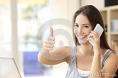 Happy girl calling on phone with thumbs up at home Stock Photo