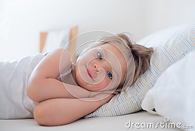 Happy girl daughter waking up smiling looking at camera on parent`s bed at morning. Happy relaxed family life with Stock Photo