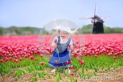 Happy girl in Dutch costume in tulips field with windmill Stock Photo