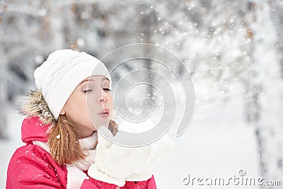 Happy girl on a frosty winter walk on street blows snow from hands Stock Photo