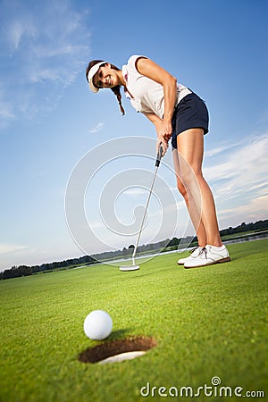 Happy girl golfer putting ball into hole. Stock Photo