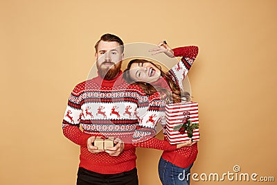 Happy girl and a guy dressed in red and white sweaters with deer hold Christmas gifts in their hands on a beige Stock Photo