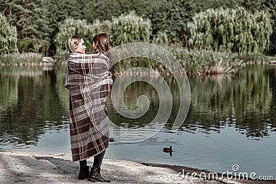 Happy, girl kisses her beautiful mother near lake are covered with blanket Stock Photo