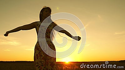 Happy girl listening to music and dancing in rays of a beautiful sunset against the sky. young girl in headphones and Stock Photo
