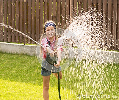 Happy girl pours water from a hose Stock Photo