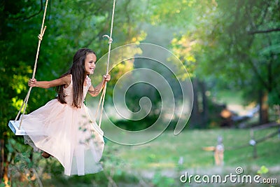 Happy girl rides on a swing in park. Little Princess has fun outdoor, summer nature outdoor. Childhood, child lifestyle, enjoyment Stock Photo