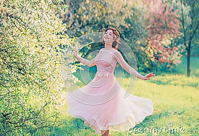 Happy girl in short flying gentle pink dress laughs joyfully, doll princess whirls in bright yellow spring garden with Stock Photo