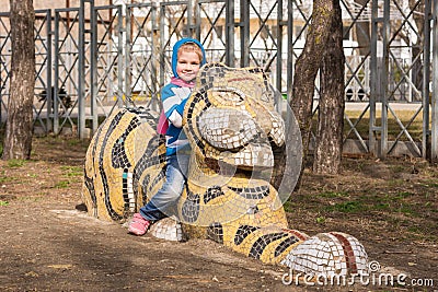 Happy girl sitting on a sculpture of a tiger on playground in Anapa Stock Photo