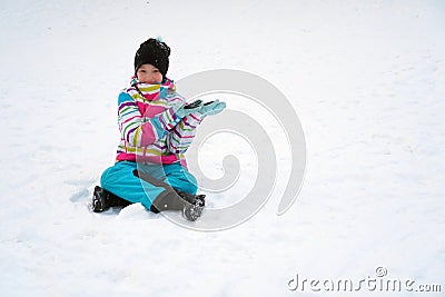 Happy girl sitting on the snow in winter. A child in a ski suit with her hands shows on copy space. Stock Photo