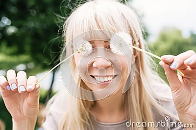 Happy girl smiling, dandelions on eyes as eyeglasses. Joyful, funny spring,summer day, outdoors Stock Photo