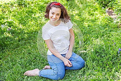 Happy girl smiling outdoor. Beautiful young brunete woman with brown hair resting on park or garden green grass background. Stock Photo