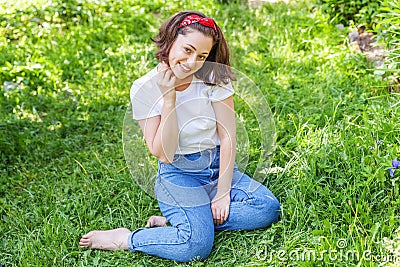 Happy girl smiling outdoor. Beautiful young brunete woman with brown hair resting on park or garden green grass background. Stock Photo