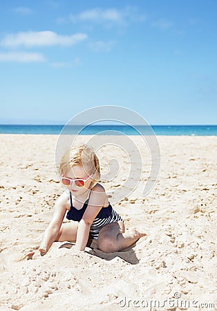 Happy girl in striped swimsuit playing with sand on white beach Stock Photo
