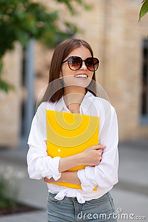 Happy girl student with a yellow folder in his hands. Exams, optimistic startup. Future achievements and ambitions Stock Photo