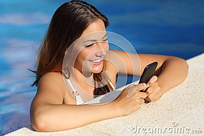 Happy girl using a smart phone in a swimming pool in summer vacations Stock Photo