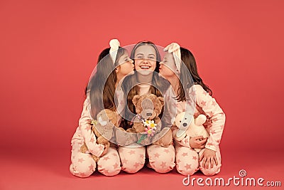 Happy girls in pyjamas kissing elder sister sitting together with teddy bears, sisterly love. Stock Photo