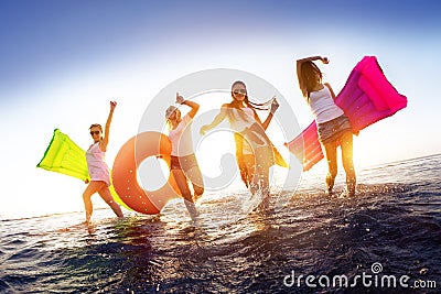 Happy girls walking in sunset water with swimming mattresses Stock Photo