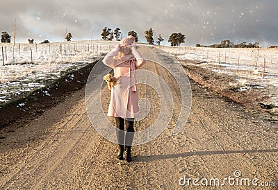 Happy go lucky woman walking down dirt road in light snow fall Stock Photo