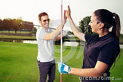 Happy golf player couple giving high five while standing on field Stock Photo