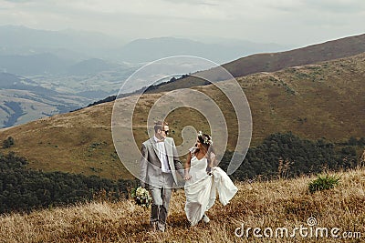 Happy gorgeous bride and groom walking in sun light holding han Stock Photo