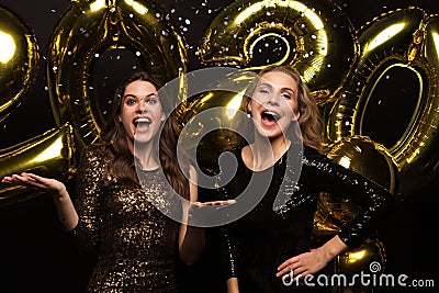 Happy gorgeous girls in stylish sexy party dresses holding gold 2020 balloons, having fun at New Year`s Eve Party Stock Photo