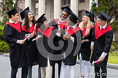Happy graduates in graduation costumes chatting during ceremony Stock Photo
