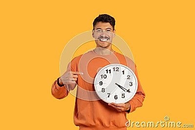 Happy guy with clock showing punctuality on yellow Stock Photo