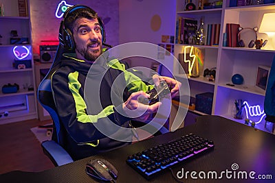 Happy guy gamer wear headphone play video game colorful neon lights computer in living room. Stock Photo