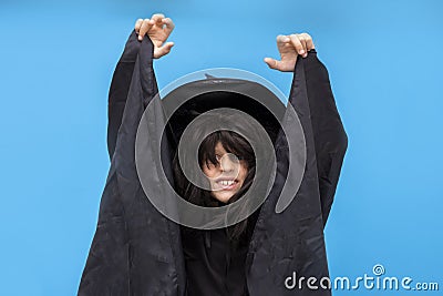 Happy Halloween kid raises his hands up while casting a spell. Child in black sorcerer& x27;s costume. Witch on blue Stock Photo