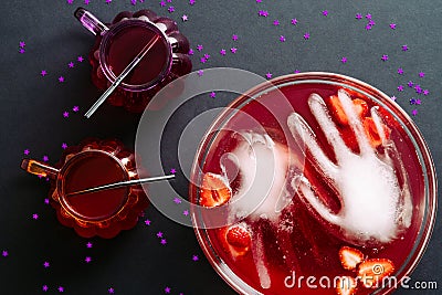 Happy Halloween party flat lay composition. Bowl of bloody color drink, frozen hands, cocktails glasses on black background. Top Stock Photo