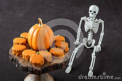 Happy Halloween, small pumpkin cakes, orange ceramic pumpkin on a wooden cake stand, plastic skeleton Stock Photo