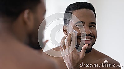 Happy handsome African American man applying moisturizer on face Stock Photo
