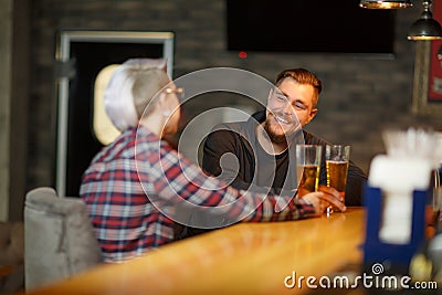 A happy guy, sitting and talking in a bar with a girl, drinking beer and laughing. Indoors. Stock Photo