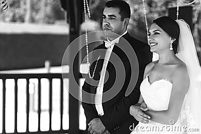Happy handsome groom and beautiful bride in white dress in wedding arbor at ceremony b&w Stock Photo