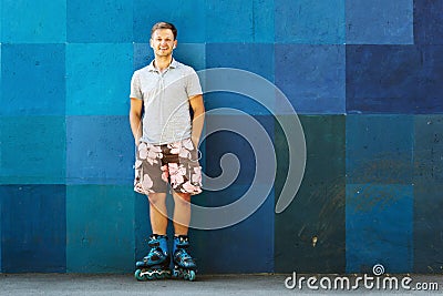 Happy handsome young roller in inline skates sitting against blu Stock Photo