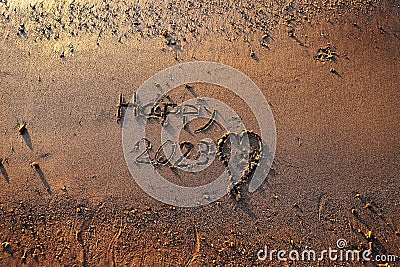 Happy 2023 handwritten on the sand of the beach with a nice side lighting, image taken from above. Concept of holiday, festivity, Stock Photo