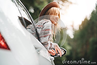 Happy hipster girl traveling adventure vacations. Boho woman sitting in car looking from window on view in country road Stock Photo