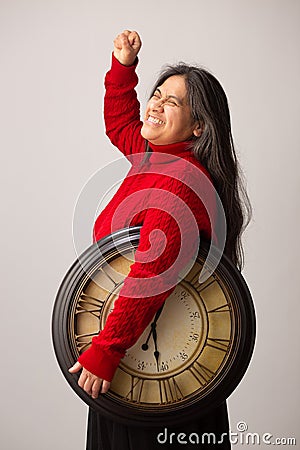 Happy Hispanic Woman With Clock Under Arm Lifts Fist In Triumph Stock Photo